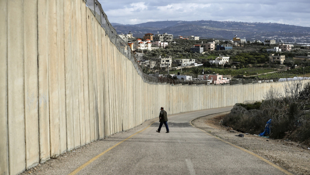 A man walks along a road by Israel's separation barrier between the occupied West Bank village of Na